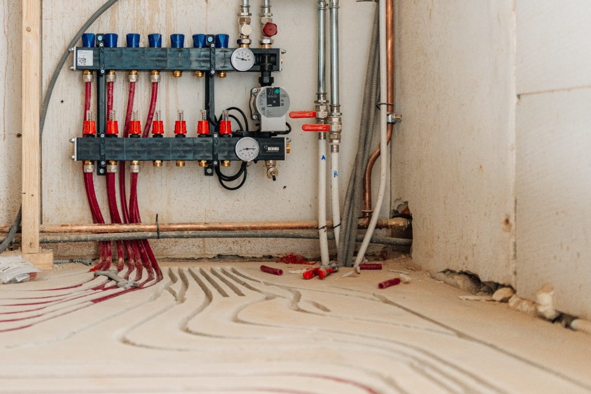 Detailfoto van een geïnstalleerde vloerverwarming met zichtbare verdeler en gefreesde sleuven voor de verwarmingsbuizen